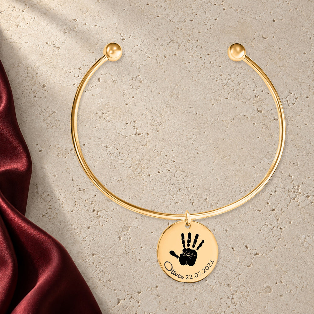 Bracelet jonc Empreinte de Main Réelle Gravée en finition dorée sur pierre claire, avec étoffe rouge sanguine ; exemple de personnalisation.