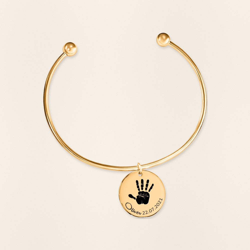 Bracelet jonc Empreinte de Main Réelle Gravée en finition dorée, exemple de gravure sur fond ivoire texturé.