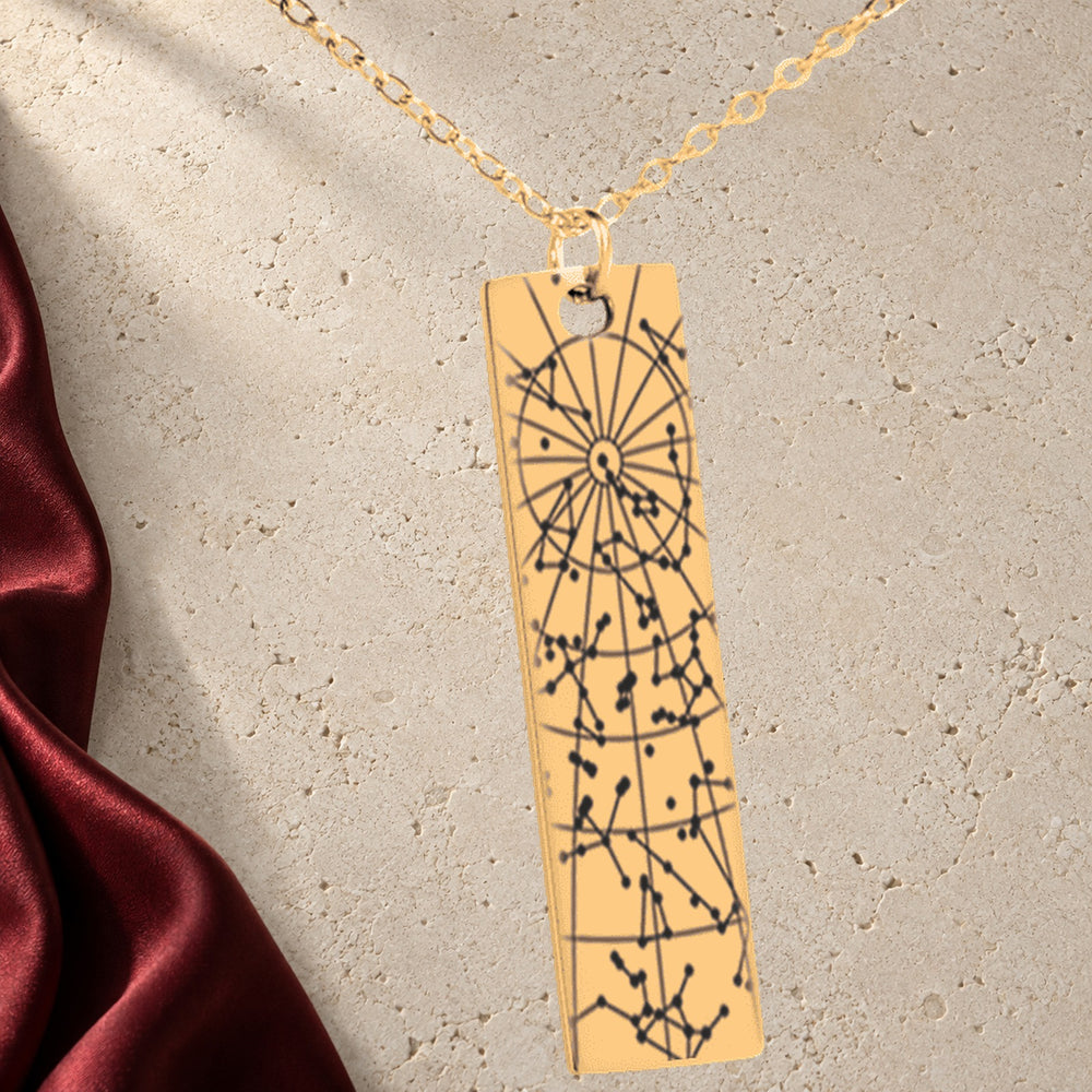 Collier Carte des Étoiles Personnalisé (Barre Verticale) en finition dorée sur pierre claire, avec étoffe rouge sanguine ; exemple de personnalisation.