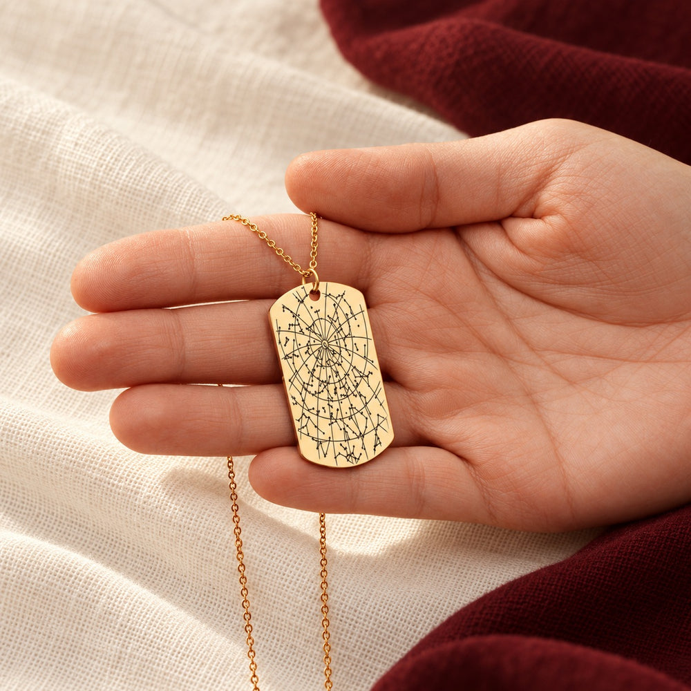 Collier Carte des Étoiles doré tenu en main, détail du pendentif gravé.