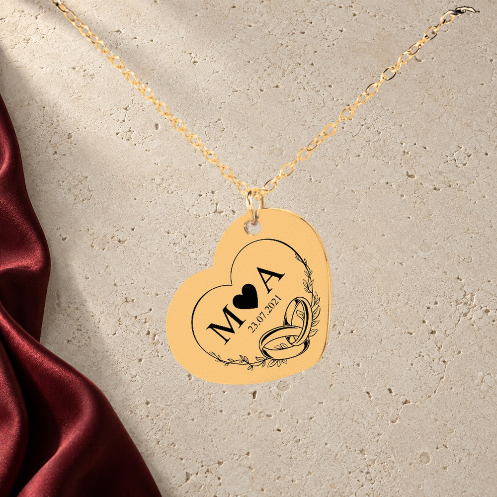 Collier Initiales Entrelacées Personnalisé (Timeless Bond Coeur) en finition dorée sur pierre claire, avec étoffe rouge sanguine ; exemple de personnalisation.