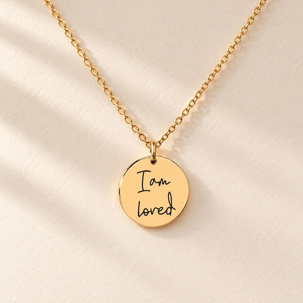 Collier Médaille Affirmations doré avec message manuscrit I am loved gravé, sur fond ivoire.