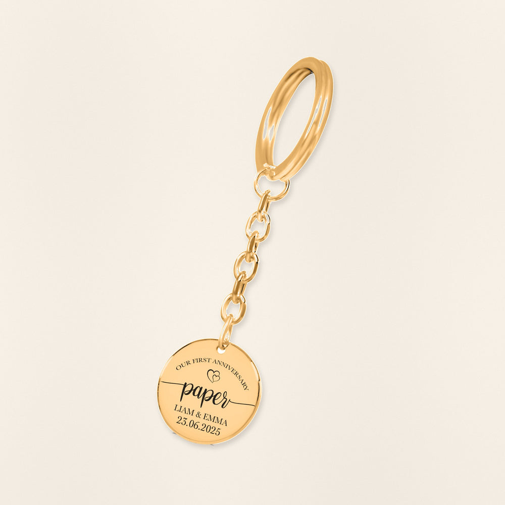 Porte-clés Médaille Anniversaire de Mariage 1 an (noces de coton) en finition dorée, exemple de gravure sur fond ivoire texturé.