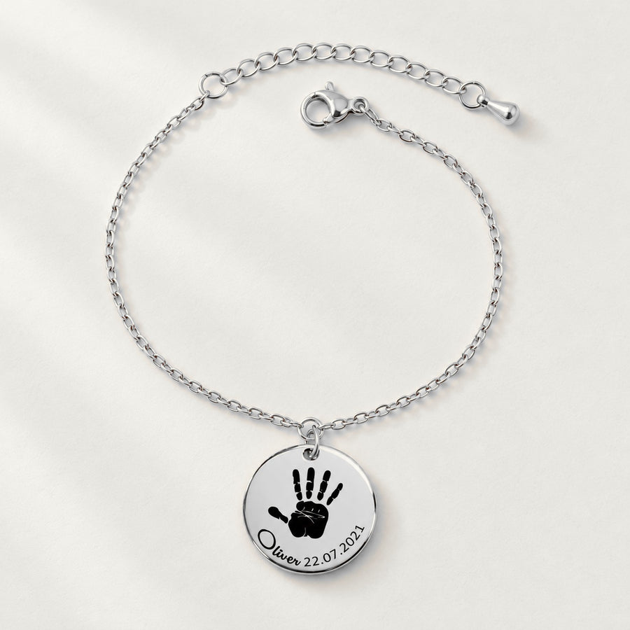 Bracelet Empreinte de Main Réelle Gravée, finition argentée, sur fond ivoire.