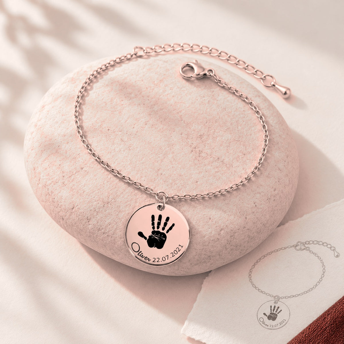 Bracelet Empreinte de Main Réelle Gravée, finition or rose, sur une pierre claire.
