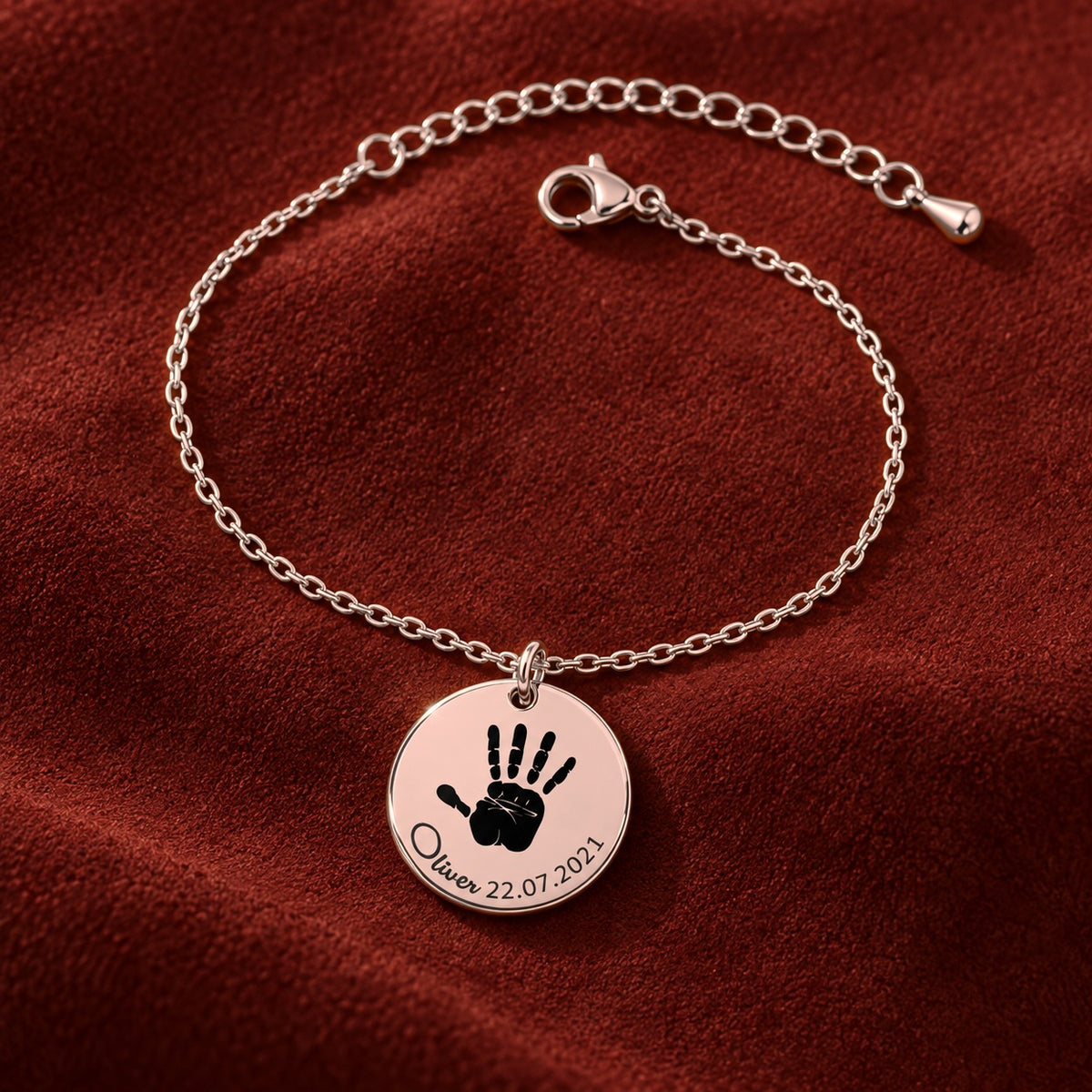 Bracelet Empreinte de Main Réelle Gravée, finition or rose, sur fond rouge sanguine.
