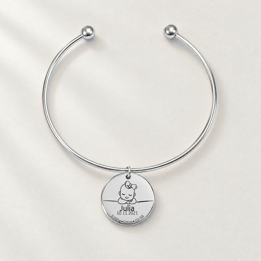 Bracelet jonc Détails de Naissance Personnalisés, finition argentée, sur fond ivoire.