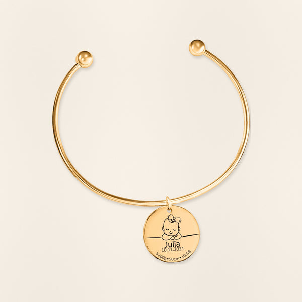 Bracelet jonc Détails de Naissance Personnalisés en finition dorée, exemple de gravure sur fond ivoire texturé.
