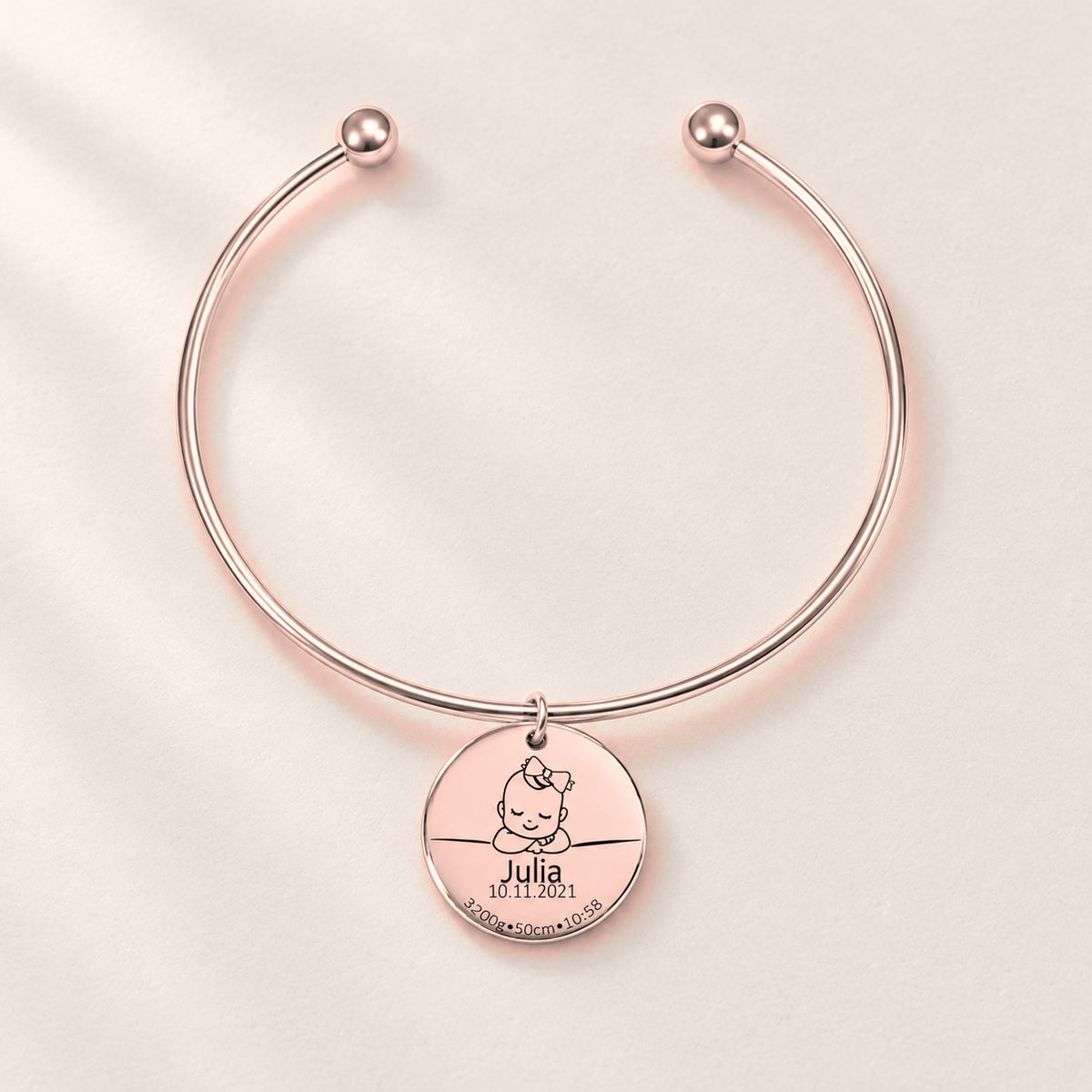 Bracelet jonc Détails de Naissance Personnalisés, finition or rose, sur fond ivoire.