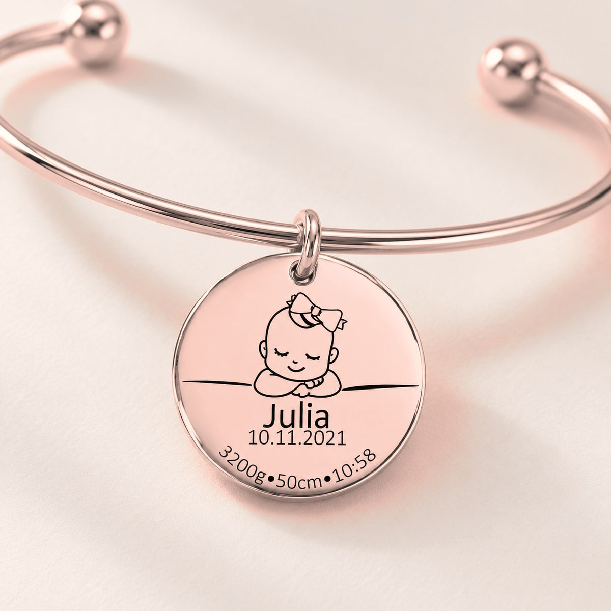 Bracelet jonc Détails de Naissance Personnalisés, finition or rose, en gros plan sur la gravure.