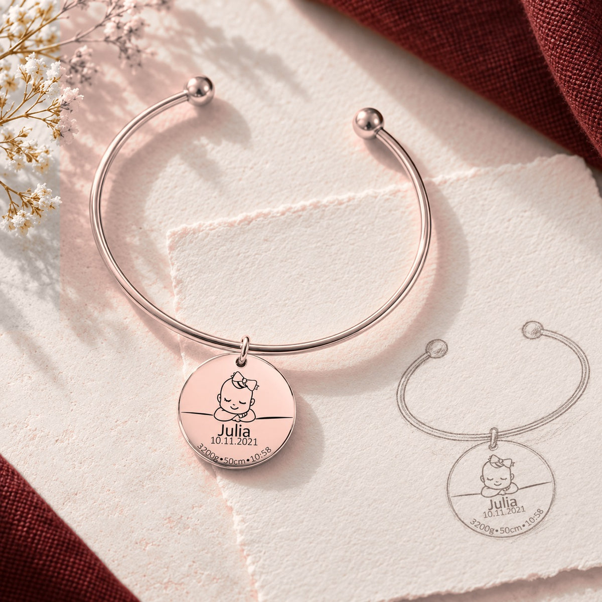 Bracelet jonc Détails de Naissance Personnalisés, finition or rose, près d’un croquis au crayon.