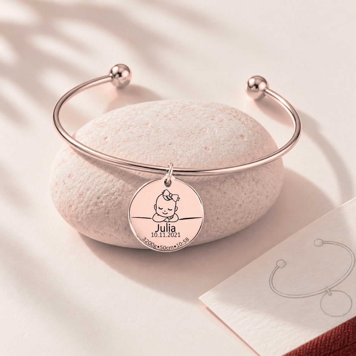 Bracelet jonc Détails de Naissance Personnalisés, finition or rose, sur une pierre claire.