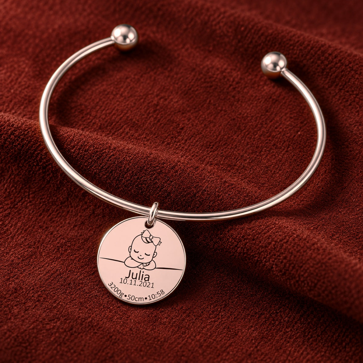 Bracelet jonc Détails de Naissance Personnalisés, finition or rose, sur fond rouge sanguine.