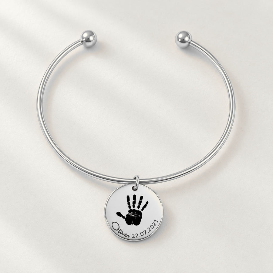 Bracelet jonc Empreinte de Main Réelle Gravée, finition argentée, sur fond ivoire.