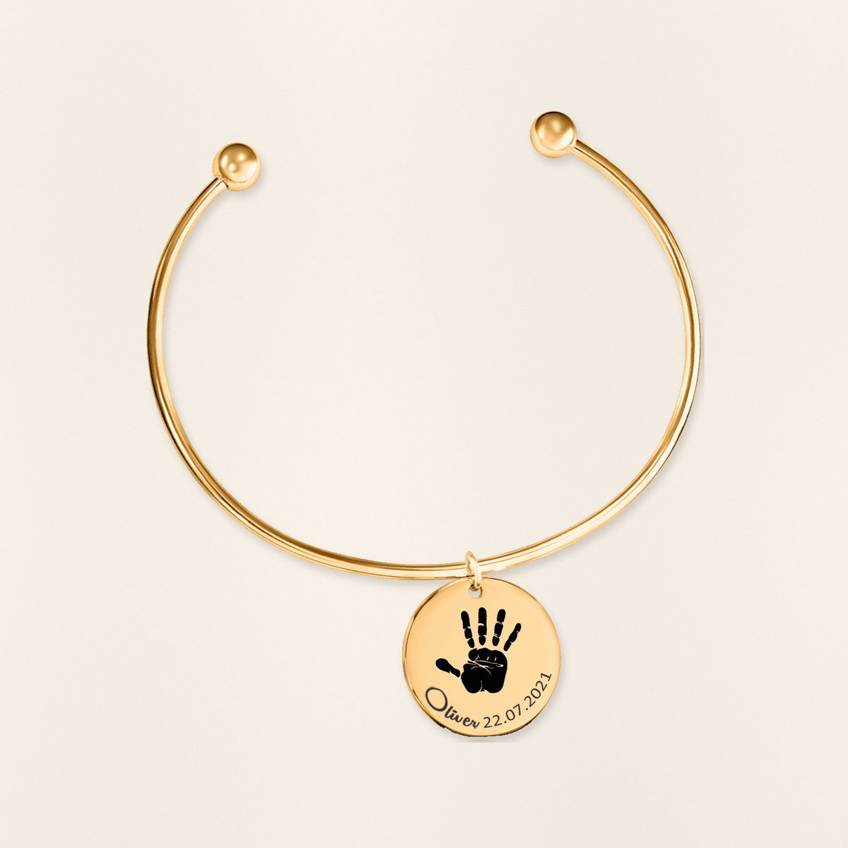 Bracelet jonc Empreinte de Main Réelle Gravée en finition dorée, exemple de gravure sur fond ivoire texturé.