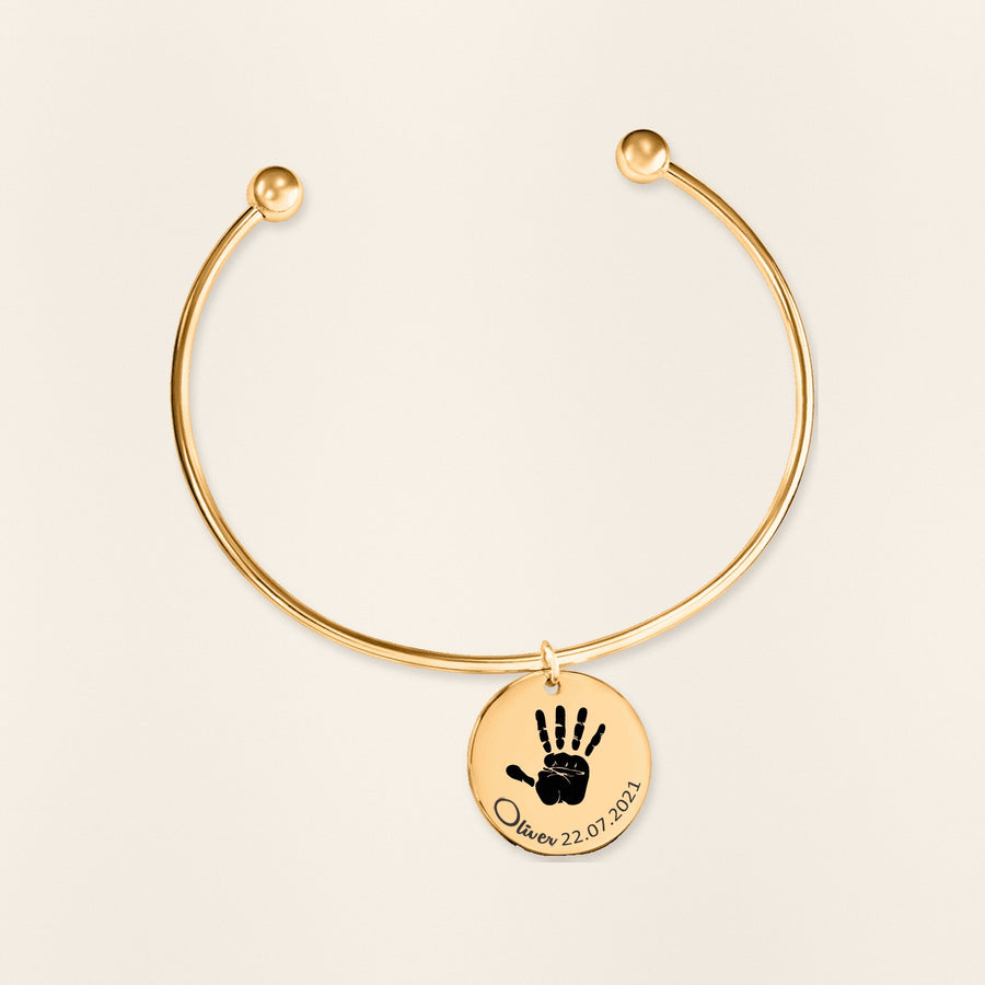 Bracelet jonc Empreinte de Main Réelle Gravée en finition dorée, exemple de gravure sur fond ivoire texturé.