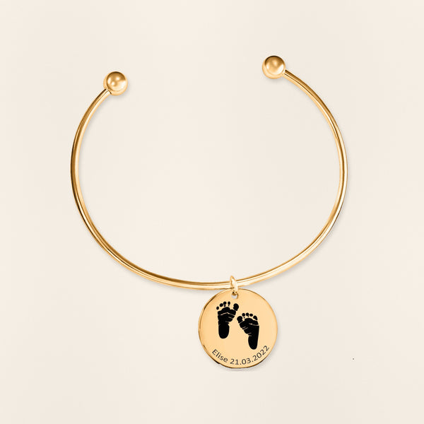 Bracelet jonc Empreinte de Pied Réelle Gravée en finition dorée, exemple de gravure sur fond ivoire texturé.