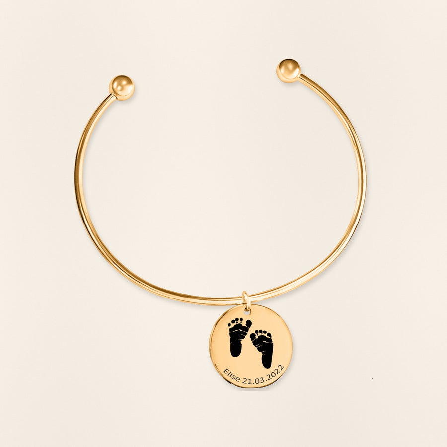 Bracelet jonc Empreinte de Pied Réelle Gravée en finition dorée, exemple de gravure sur fond ivoire texturé.