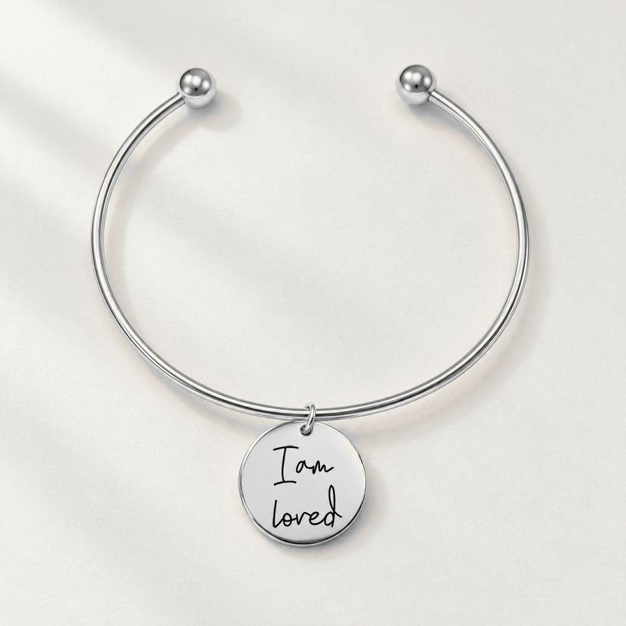 Bracelet jonc Médaille Affirmations Personnalisée, finition argentée, sur fond ivoire.