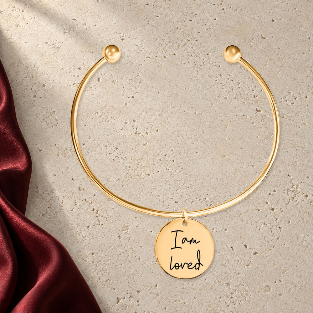 Bracelet jonc Médaille Affirmations Personnalisée en finition dorée sur pierre claire, avec étoffe rouge sanguine ; exemple de personnalisation.
