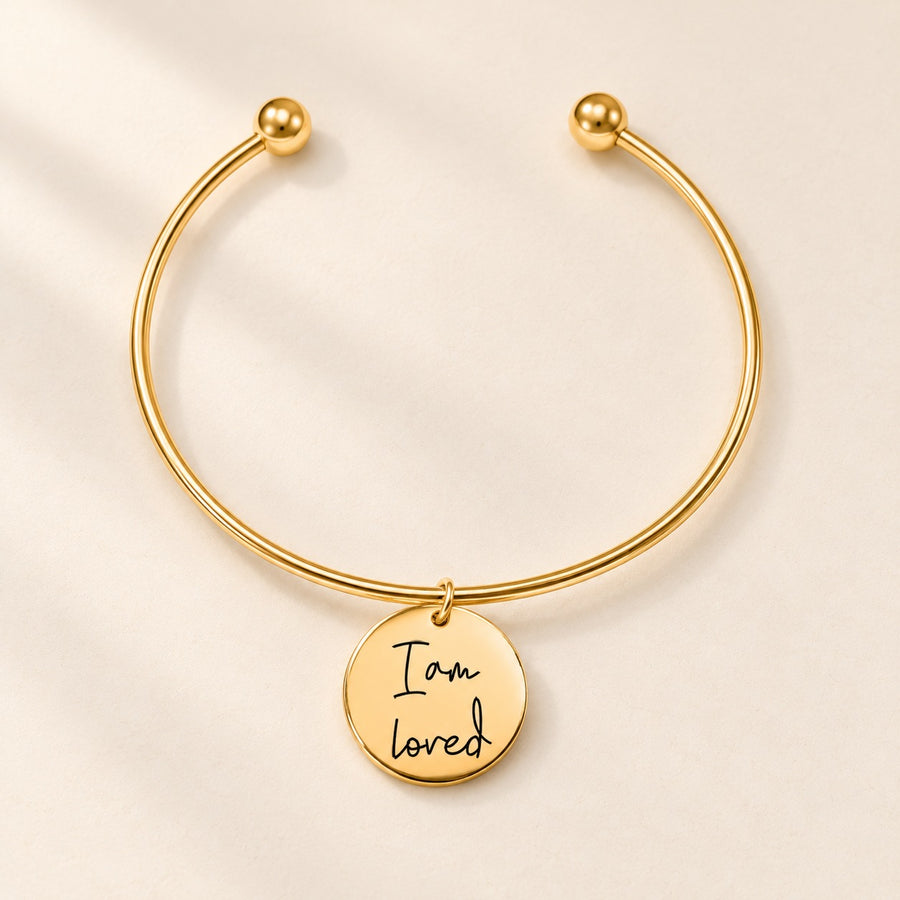 Bracelet jonc doré à médaille gravée « I am loved » sur fond ivoire.