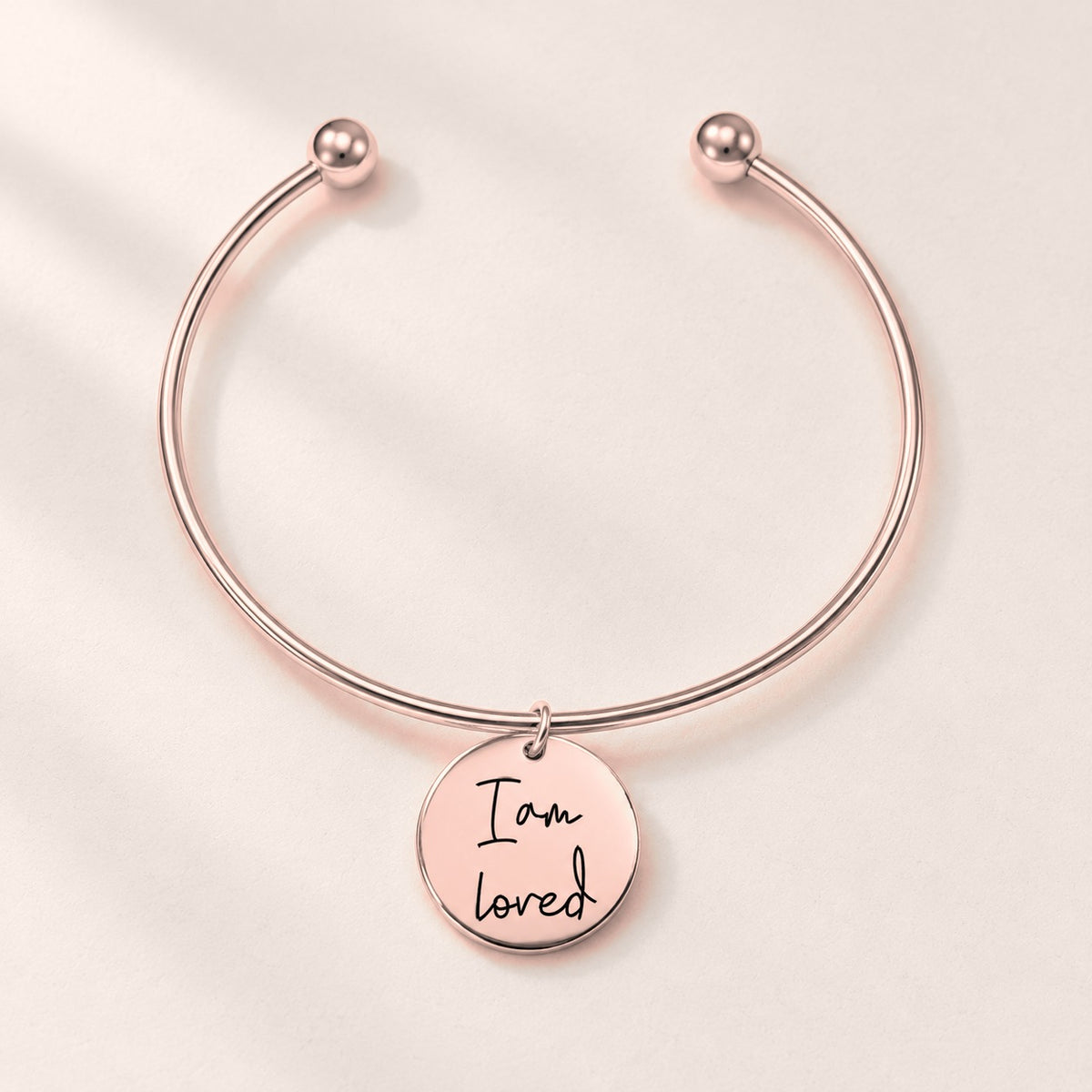 Bracelet jonc Médaille Affirmations Personnalisée, finition or rose, sur fond ivoire.