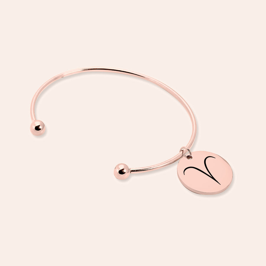 Bracelet jonc en finition or rose, médaille gravée du signe Bélier, sur fond ivoire.