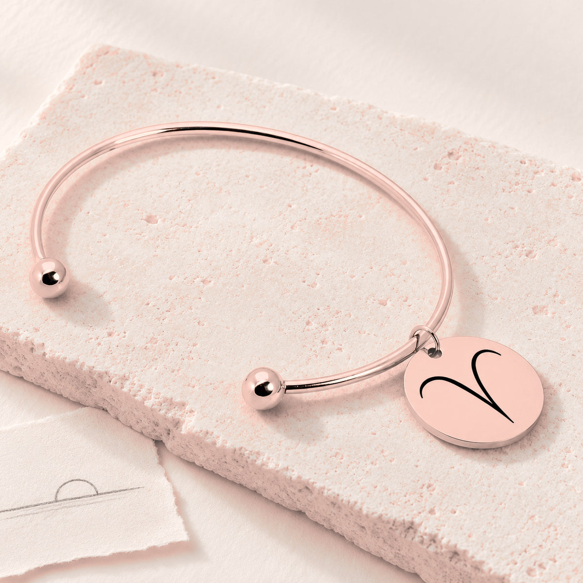 Bracelet Jonc Zodiaque, finition or rose, sur une pierre claire.