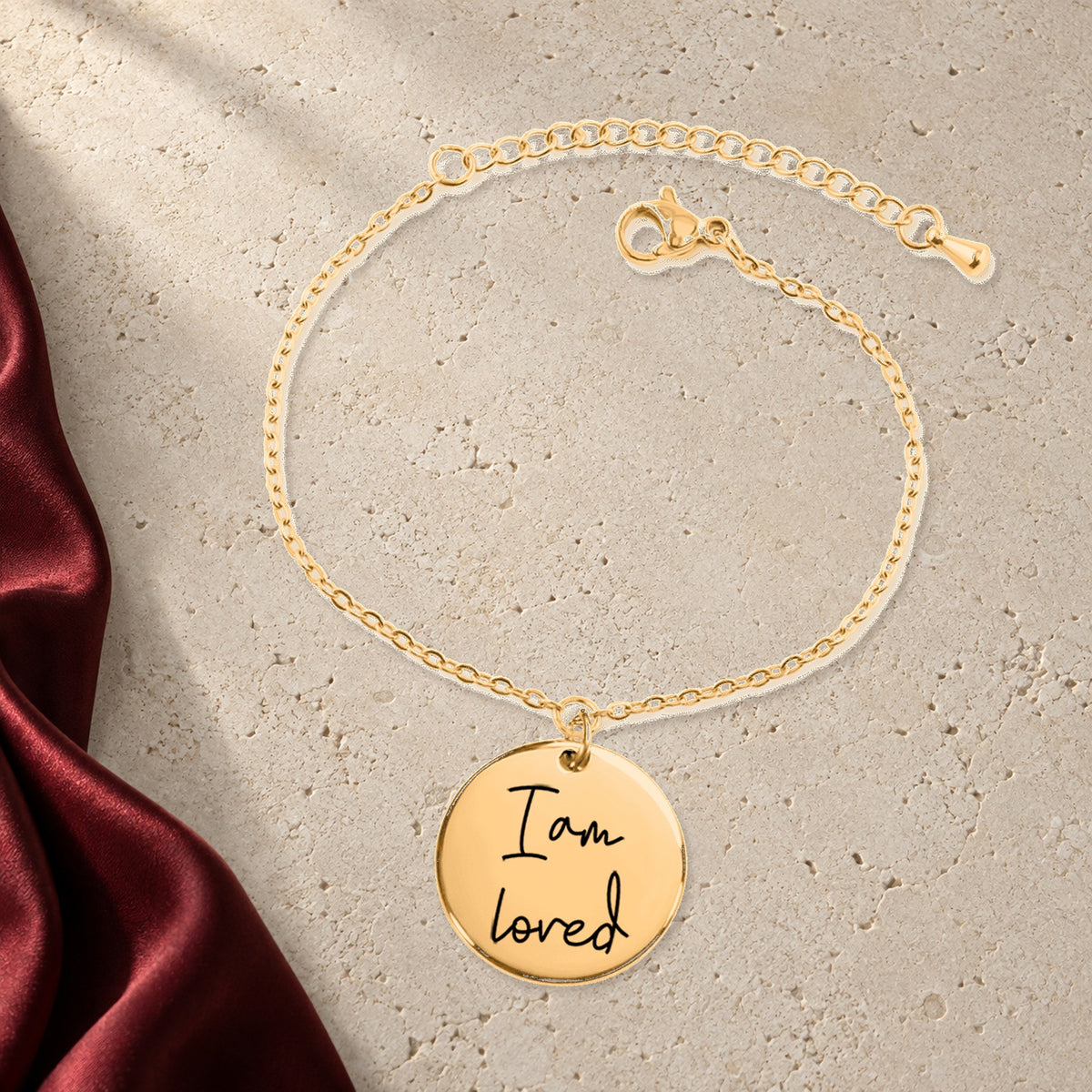 Bracelet Médaille Affirmations Personnalisée en finition dorée sur pierre claire, avec étoffe rouge sanguine ; exemple de personnalisation.