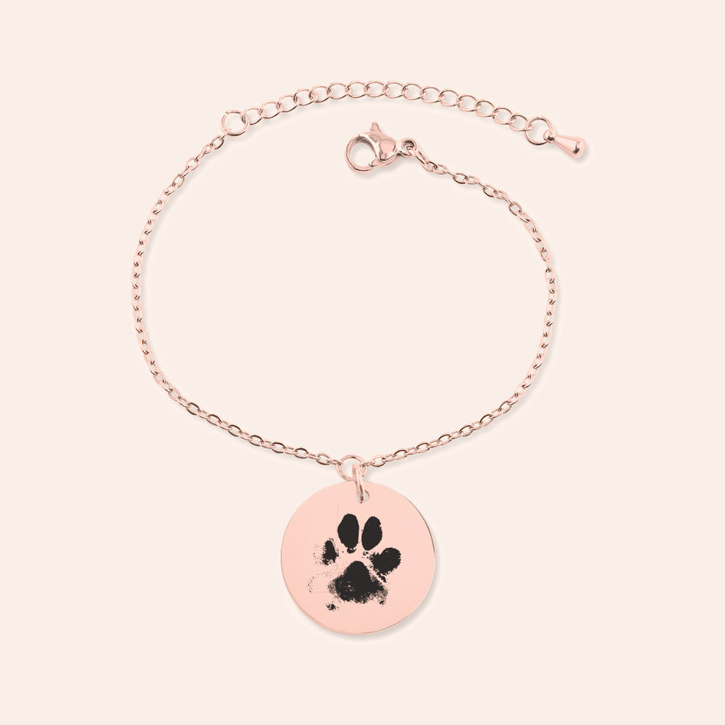 Bracelet personnalisé avec empreinte de patte, finition or rose, sur fond ivoire.