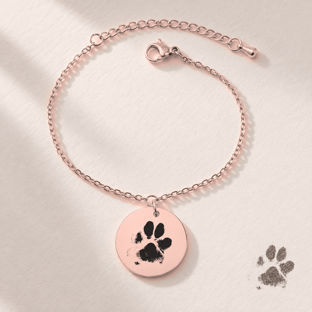 Bracelet personnalisé avec empreinte de patte, finition or rose, près d’un croquis au crayon.