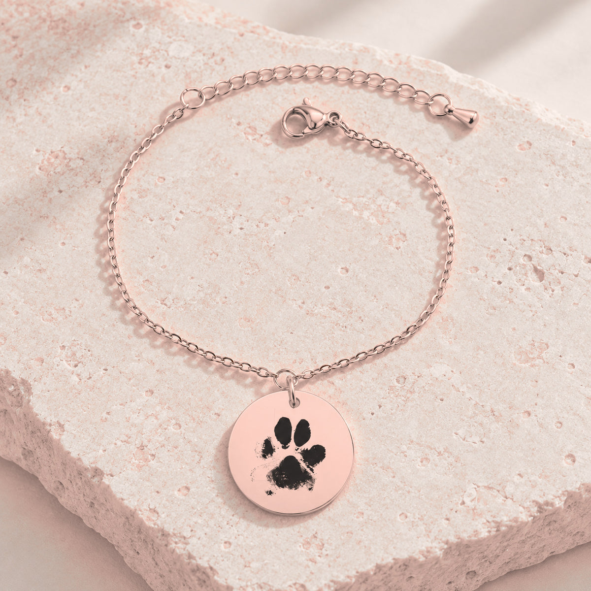 Bracelet personnalisé avec empreinte de patte, finition or rose, sur une pierre claire.