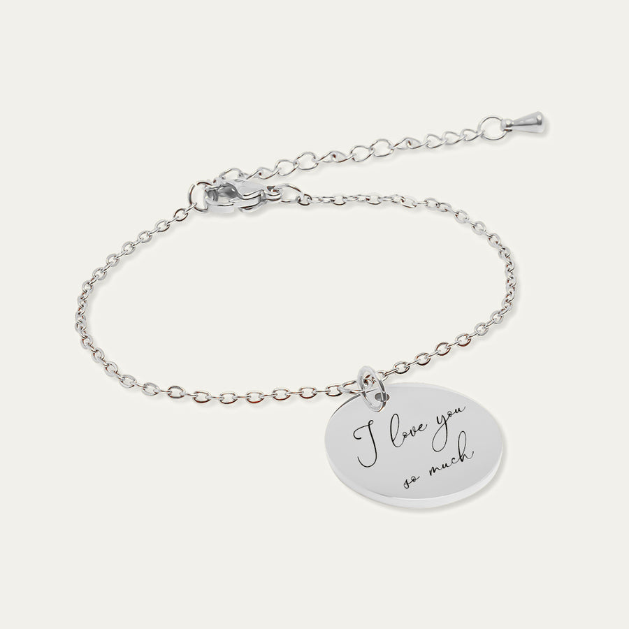 Bracelet chaîne en finition argentée, médaille gravée du message manuscrit I love you so much, sur fond ivoire.