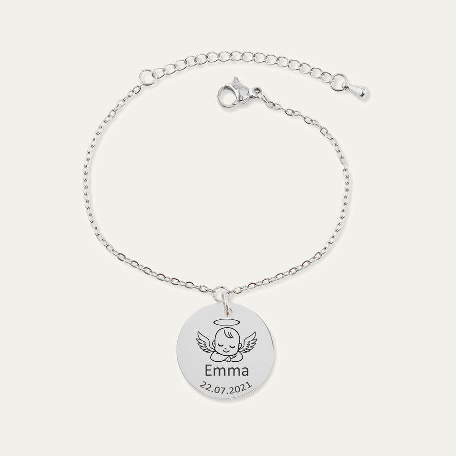 Bracelet chaîne en finition argentée, médaille gravée d’un bébé ange avec le prénom Emma et la date 22.07.2021, sur fond ivoire.