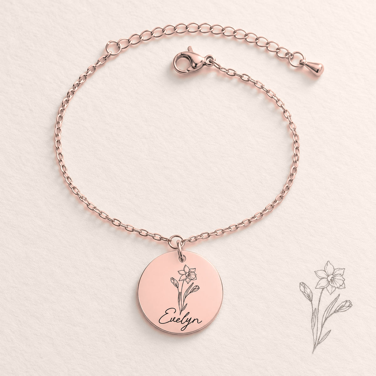 Bracelet Personnalisé de Naissance avec Fleur & Prénom, finition or rose, près d’un croquis au crayon.
