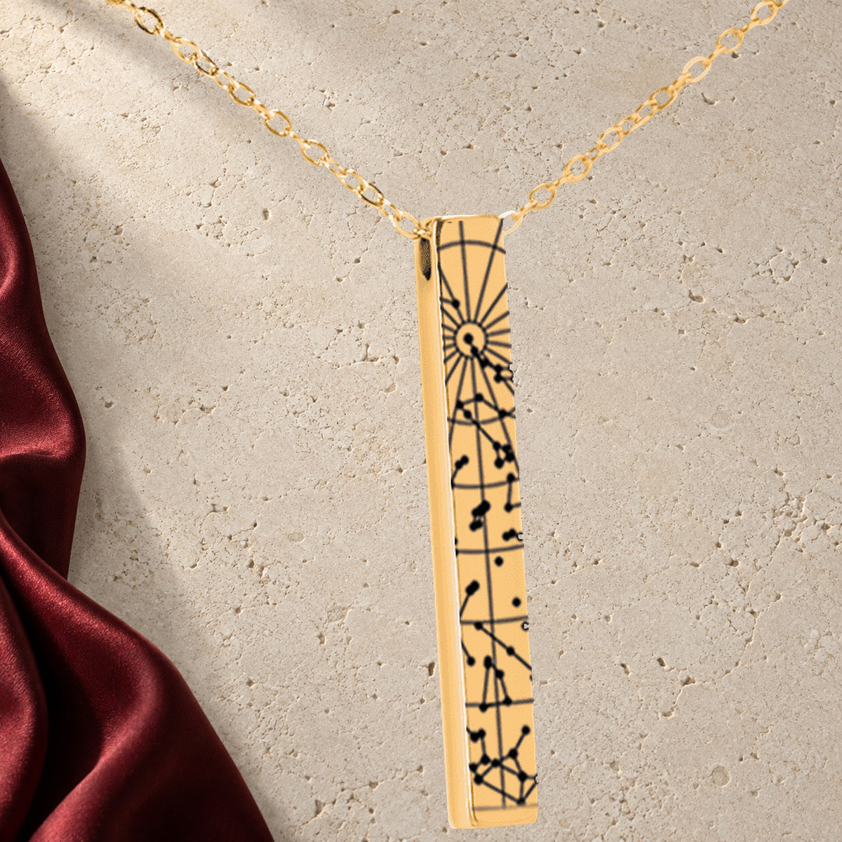 Collier Carte des Étoiles Personnalisé (Barre 3D) en finition dorée sur pierre claire, avec étoffe rouge sanguine ; exemple de personnalisation.