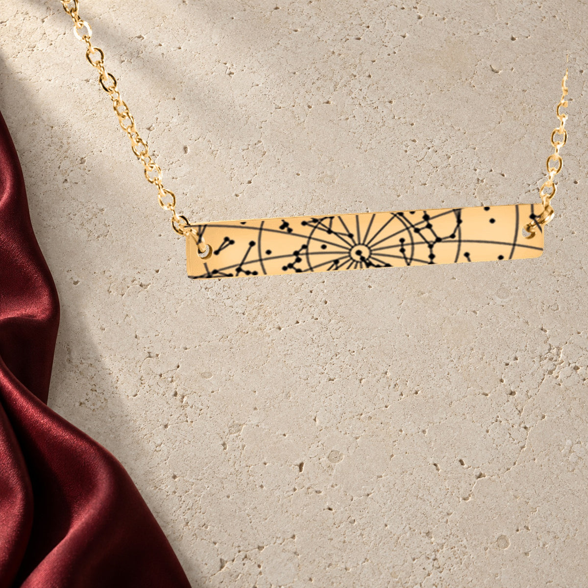 Collier Carte des Étoiles Personnalisé (Barre Horizontale) en finition dorée sur pierre claire, avec étoffe rouge sanguine ; exemple de personnalisation.