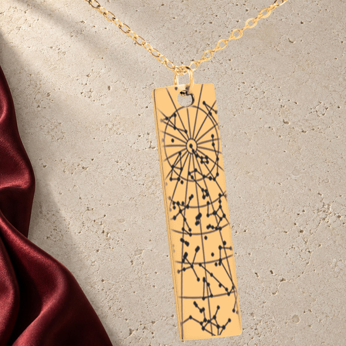 Collier Carte des Étoiles Personnalisé (Barre Verticale) en finition dorée sur pierre claire, avec étoffe rouge sanguine ; exemple de personnalisation.