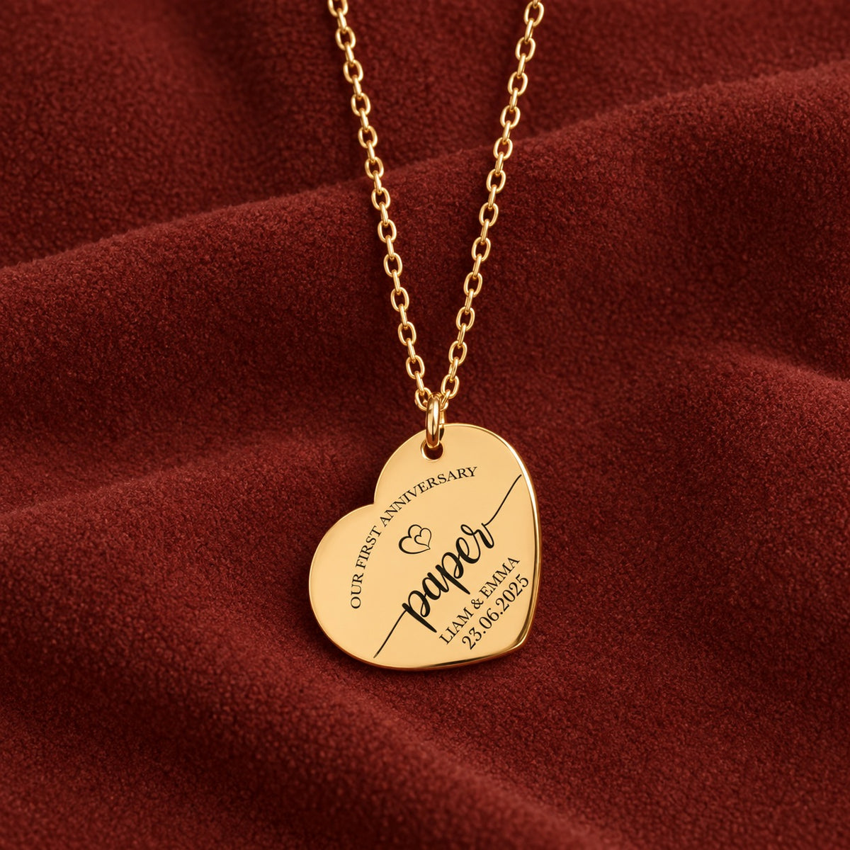 Collier cœur premier anniversaire de mariage doré avec inscription « paper », prénoms Liam et Emma et date, sur suédine rouge sanguine.