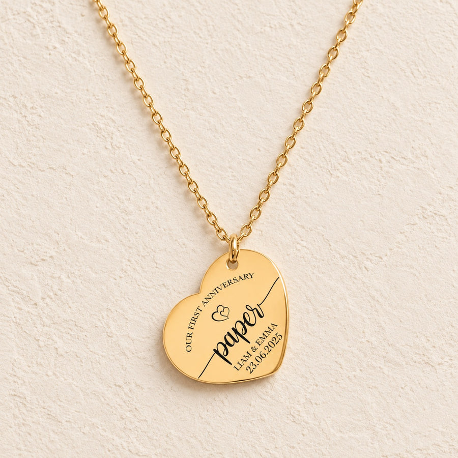 Collier cœur premier anniversaire de mariage doré avec inscription « paper », prénoms Liam et Emma et date, sur fond ivoire.