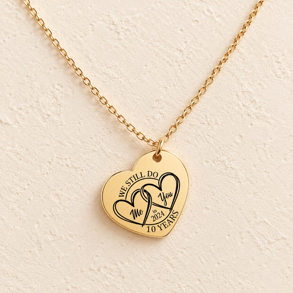 Collier cœur anniversaire de mariage 10 ans doré, médaille en cœur gravée avec deux cœurs et inscription « 10 YEARS », sur fond ivoire.