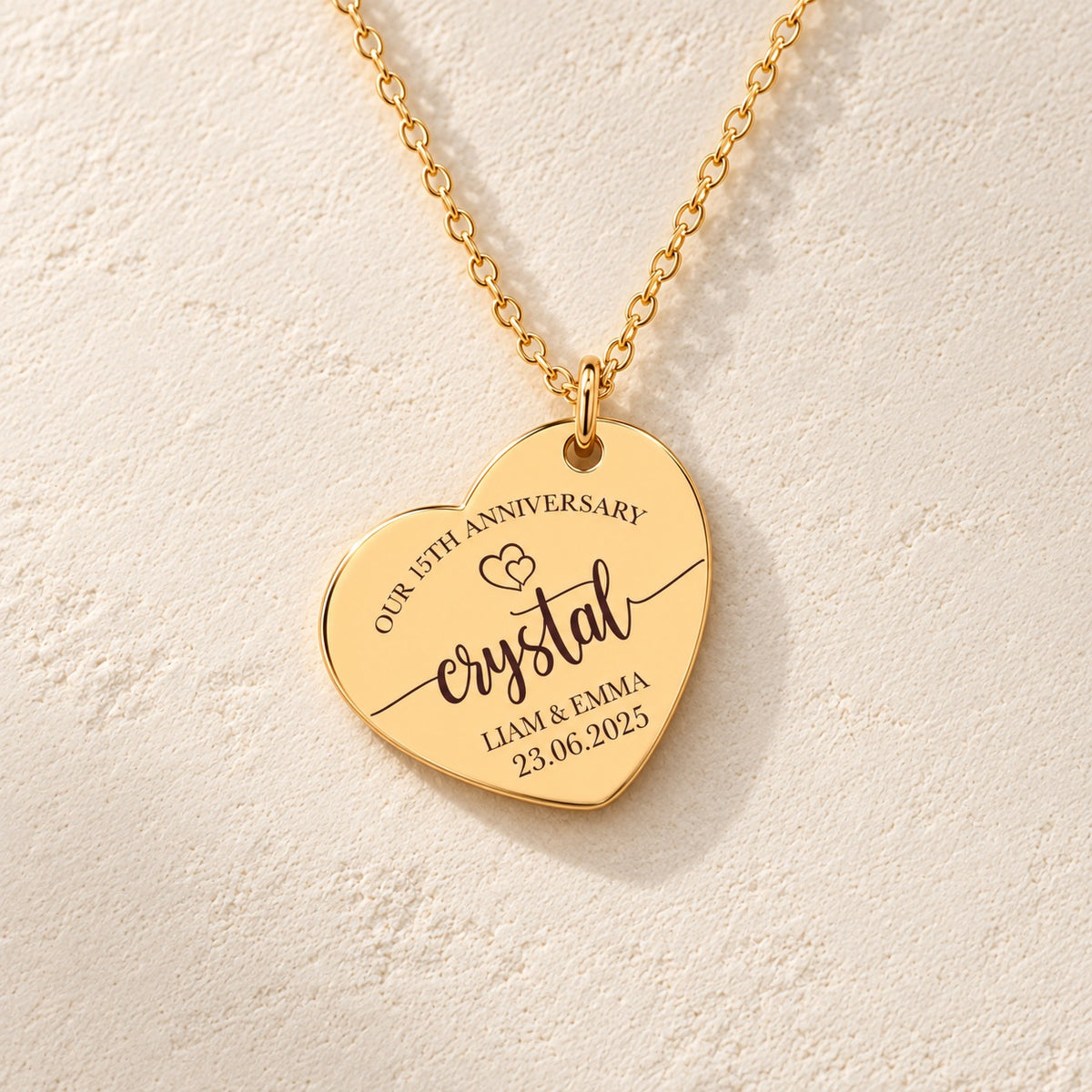 Détail de la médaille en cœur dorée avec inscription « crystal », prénoms Liam et Emma et date 23.06.2025.