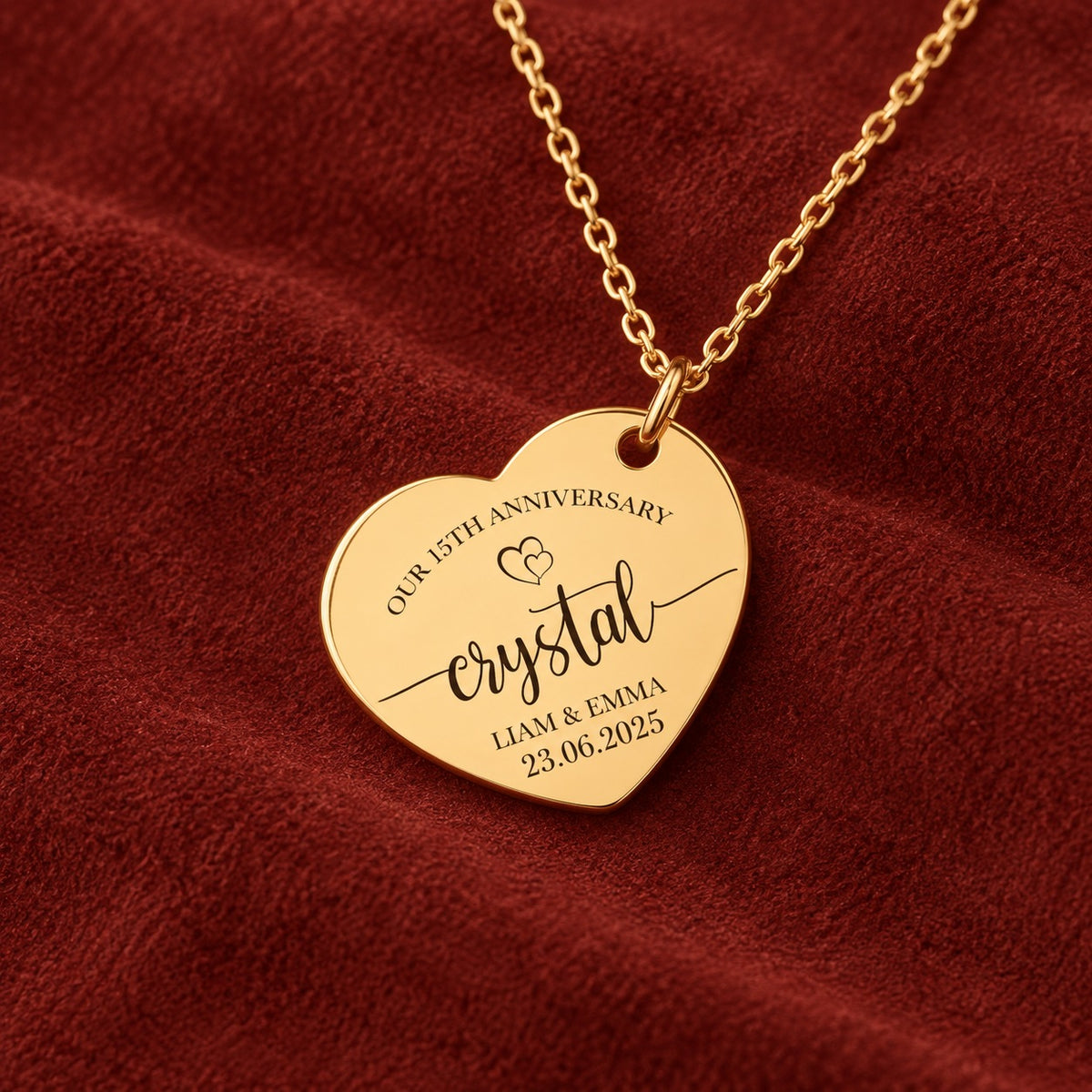 Médaille en cœur dorée avec inscription « crystal », prénoms Liam et Emma et date 23.06.2025, sur suédine rouge sanguine.