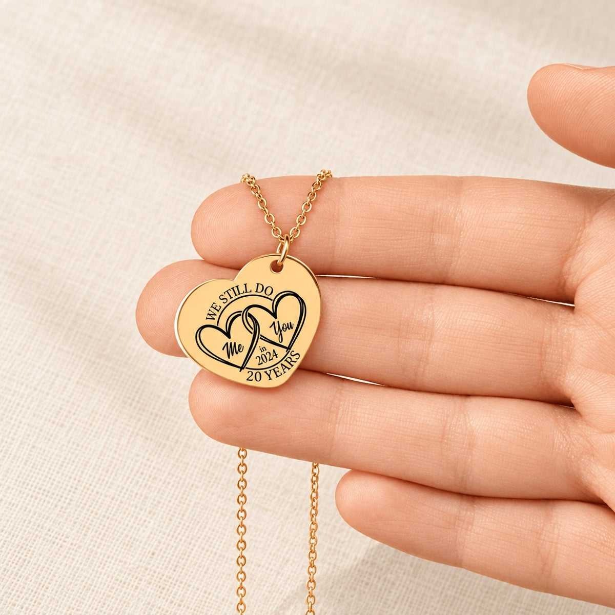 Collier Coeur Anniversaire de Mariage 20 ans doré tenu en main, détail de la gravure.