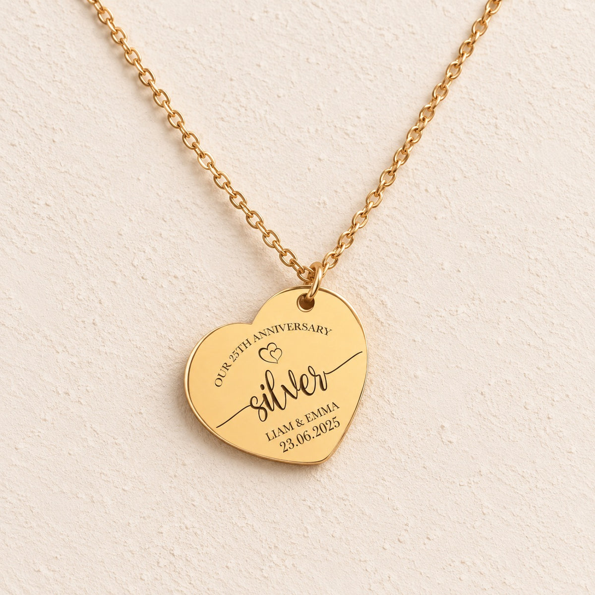 Collier cœur anniversaire de mariage 25 ans doré, médaille en cœur gravée avec inscription « silver », prénoms Liam et Emma et date 23.06.2025, sur fond ivoire.