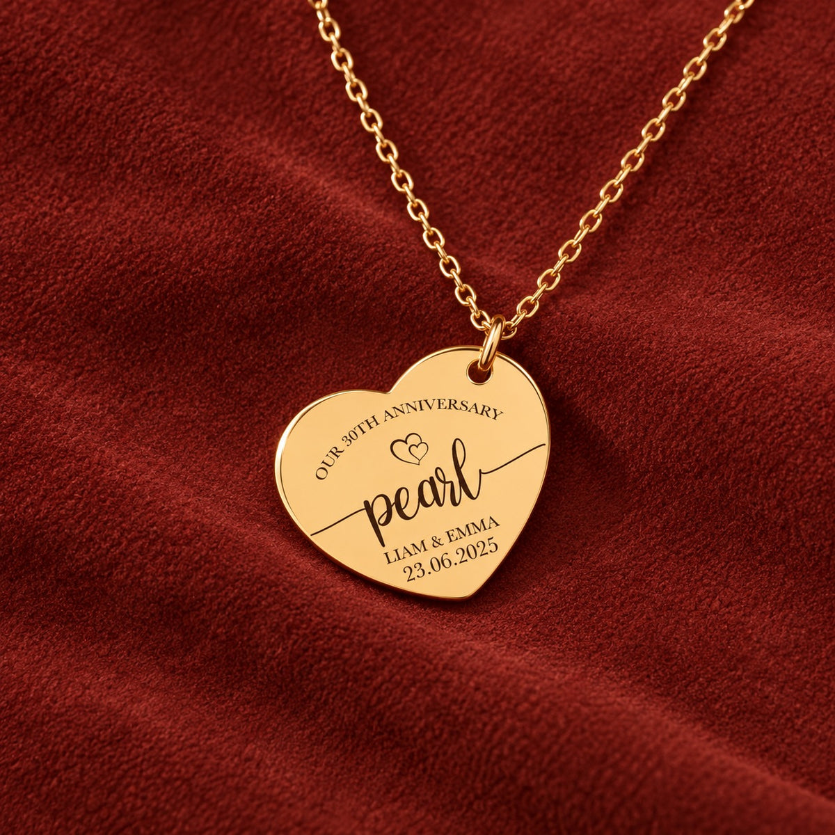 Médaille en cœur dorée avec inscription « pearl », prénoms Liam et Emma et date 23.06.2025, sur suédine rouge sanguine.