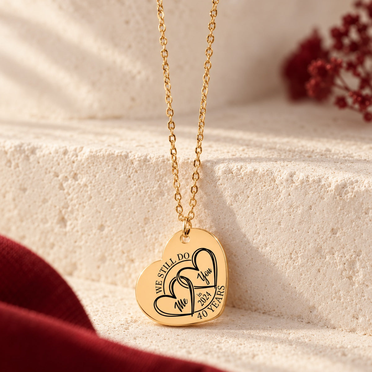 Détail du pendentif en forme de cœur doré avec deux cœurs entrelacés et inscription « 40 YEARS », sur fond ivoire.