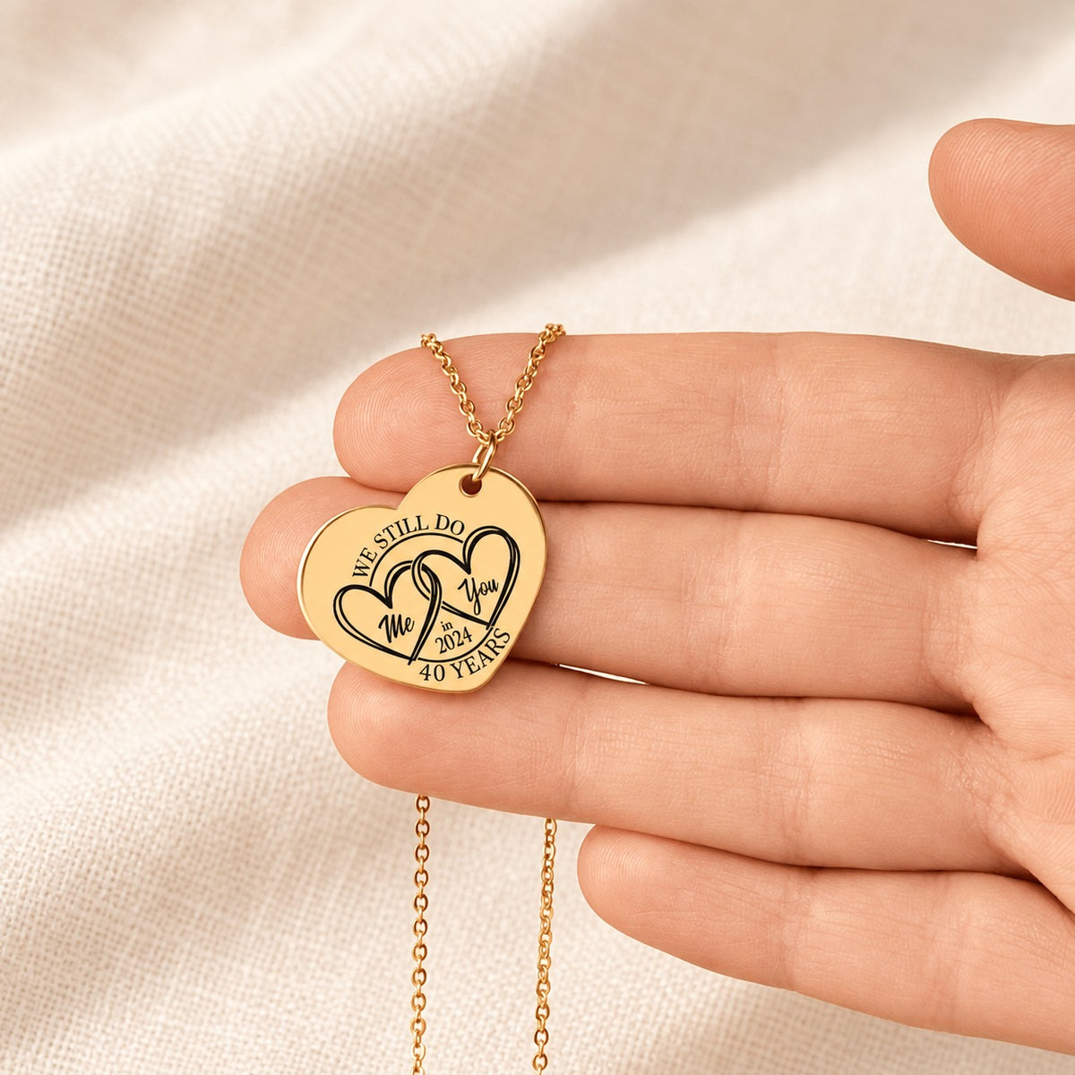 Collier cœur anniversaire de mariage 40 ans doré tenu en main, détail du pendentif et de sa gravure.
