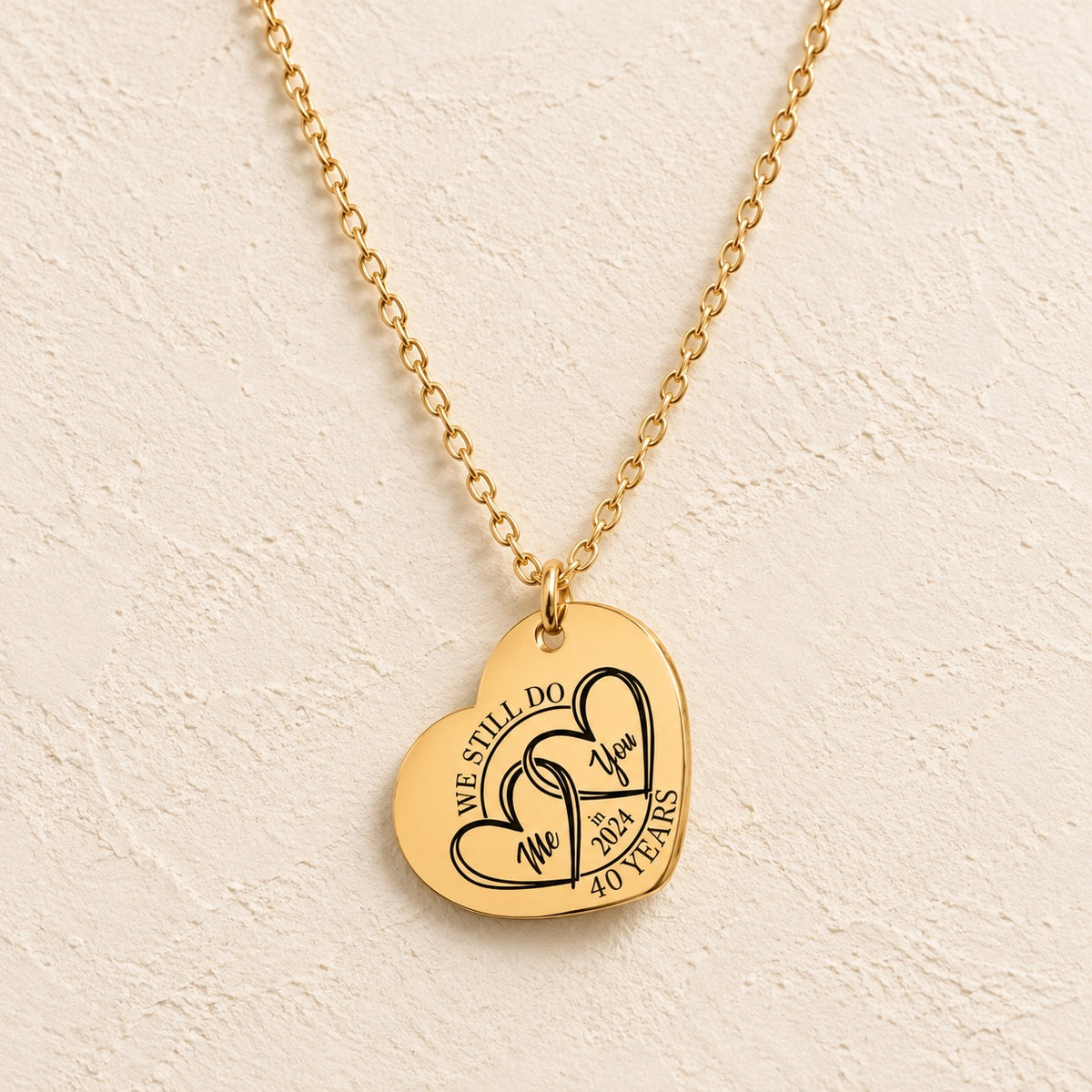 Collier cœur anniversaire de mariage 40 ans doré avec deux cœurs entrelacés et inscription « 40 YEARS », sur fond ivoire.
