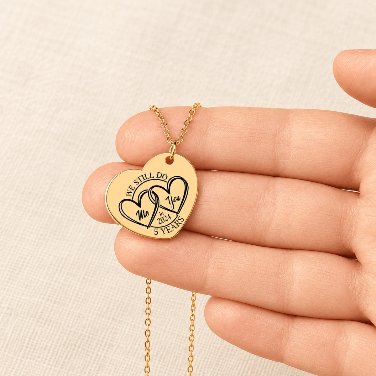 Collier Coeur Anniversaire de Mariage 5 ans doré tenu en main, détail de la gravure.